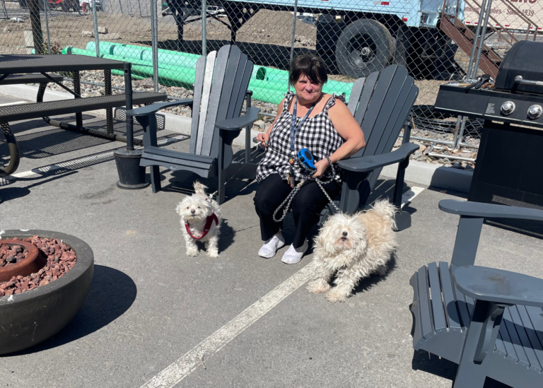 a marvel way resident with her two pet dogs, sitting at a firepit outside the supportive apartment complex
